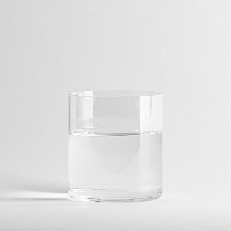 Vaso transparente cilíndrico de cristal que contiene agua, sobre fondo blanco uniforme