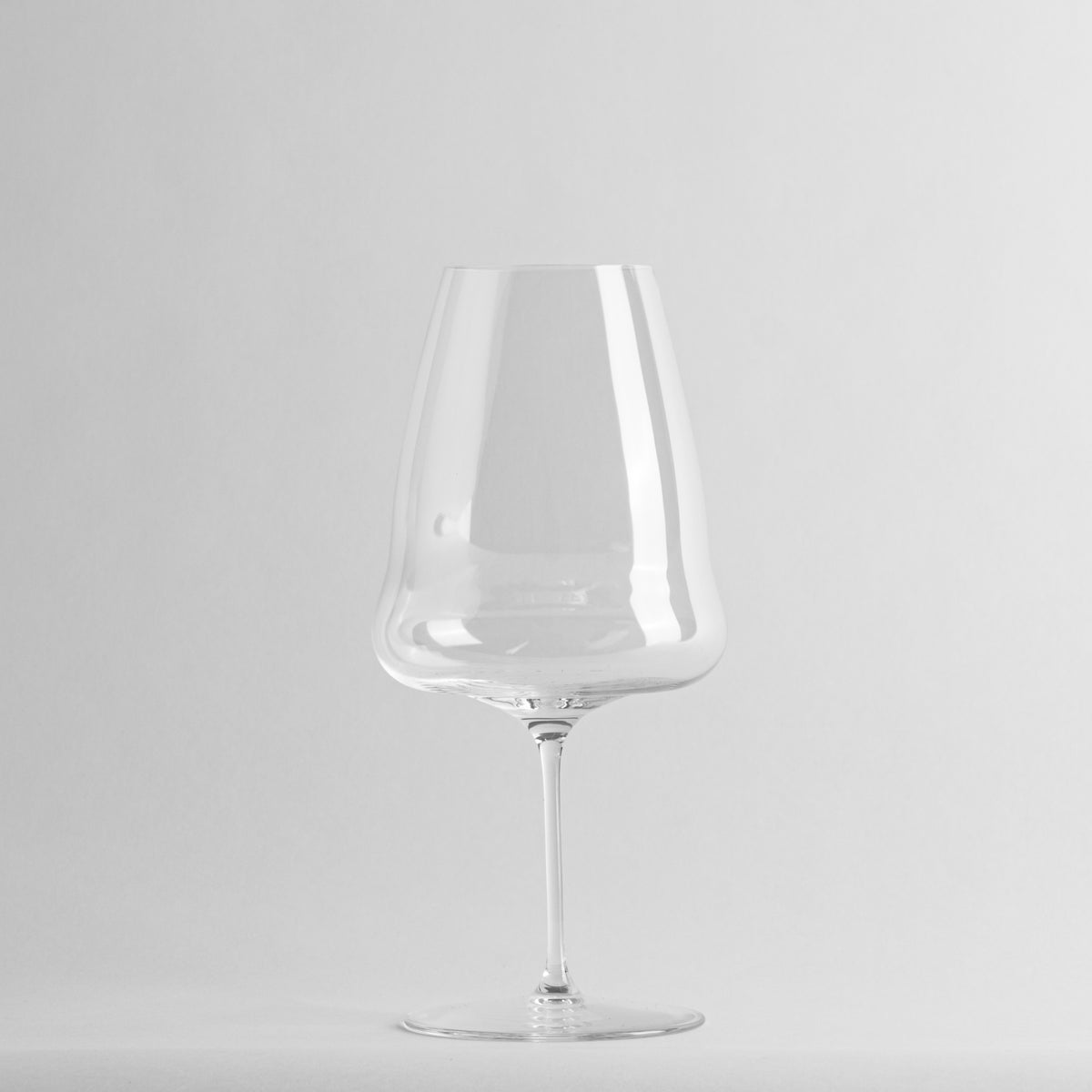 Transparent wine glass, elegant shape with slim base, rounded bottom and glossy surface, on white background.