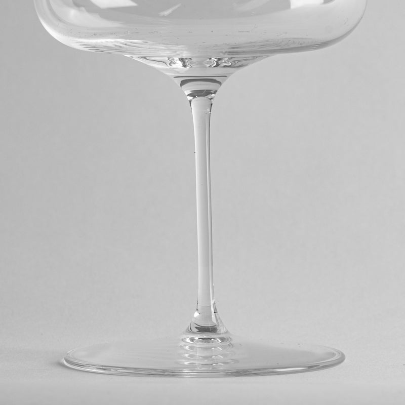 Transparent glass wine glass with thin stem and circular base on light grey background