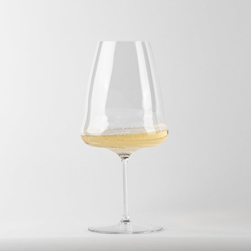 transparent glass tumbler with flat base and long stem, contains light yellow liquid with foam