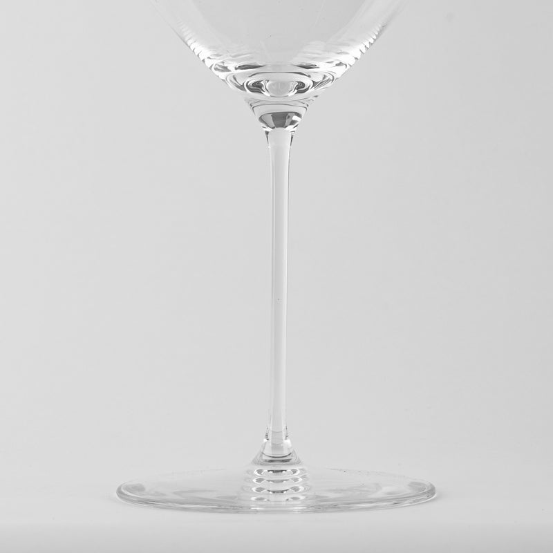 Copa de vidrio transparente con tallo fino y base redonda sobre fondo gris claro