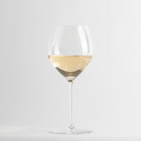 Copa de vino de vidrio transparente con vino blanco claro, fondo gris claro uniforme.