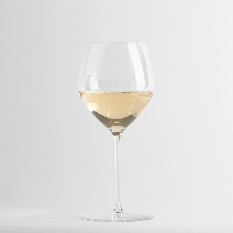 Copa de vino de vidrio transparente con vino blanco claro, fondo gris claro uniforme.