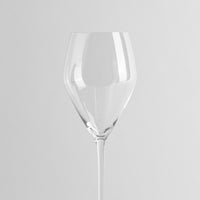 Vaso transparente de cristal con tallo largo y copa de forma redondeada, fondo gris claro uniforme