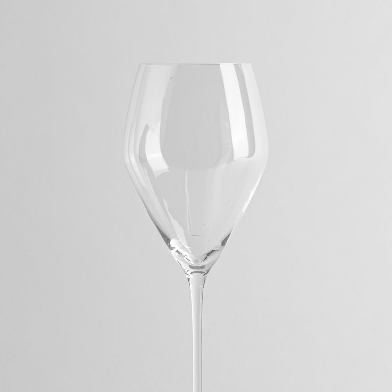 Vaso transparente de cristal con tallo largo y copa de forma redondeada, fondo gris claro uniforme
