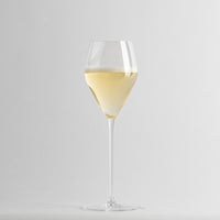 Copa de vino de vidrio transparente que contiene vino blanco espumoso sobre fondo gris claro uniforme.