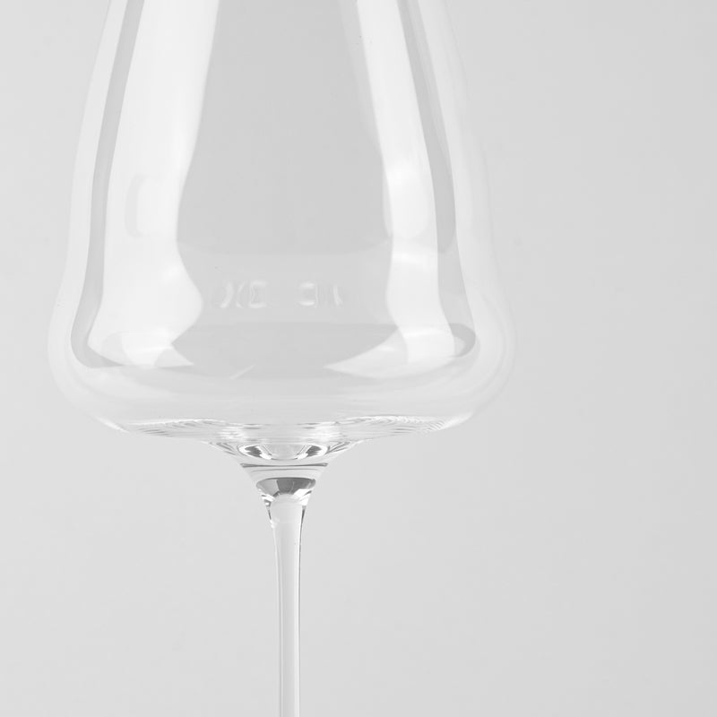 Verre à vin en verre transparent à tige fine sur fond clair uniforme.