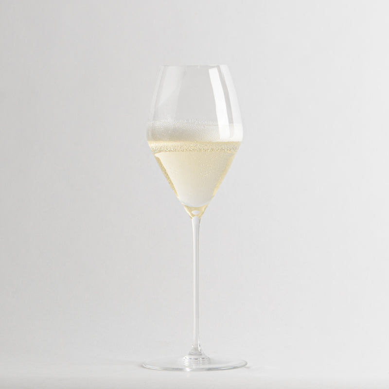 Calice di vetro trasparente con liquido giallo chiaro frizzante su sfondo neutro chiaro.