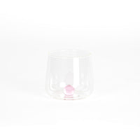 bicchiere trasparente in vetro con base arrotondata contenente una sfera rosa al centro, su sfondo bianco uniforme