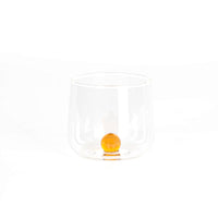 bicchiere trasparente in vetro con base arrotondata e sfera arancione all'interno su sfondo bianco chiaro
