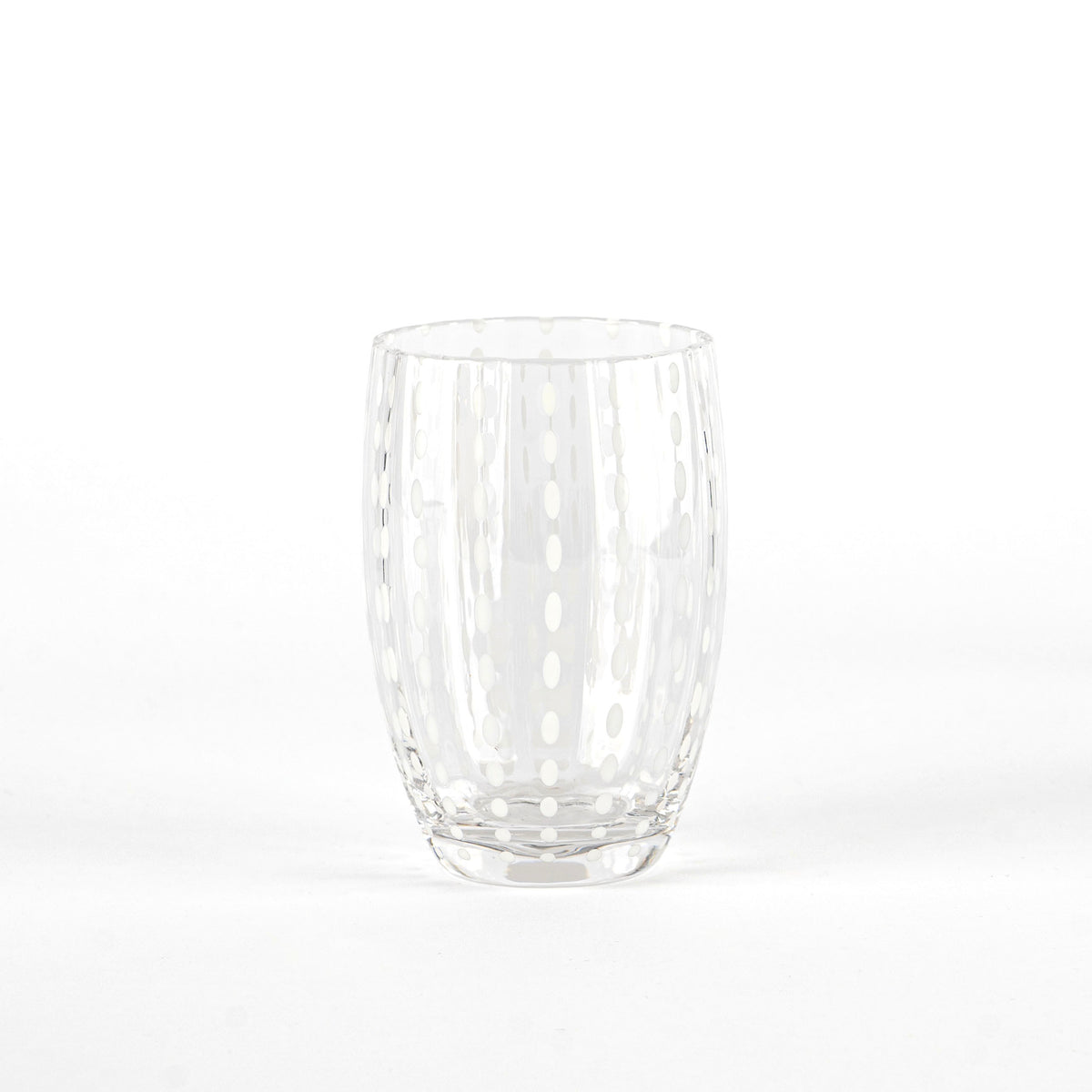 Transparent glass tumbler with vertical white oval decorations, neutral white background and surface.