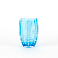 Transparent light blue glass tumbler with white dot decorations, oval design, on white background.