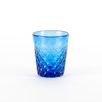 Verre turquoise en verre avec surface facettée et motifs en losange, sur fond blanc neutre.