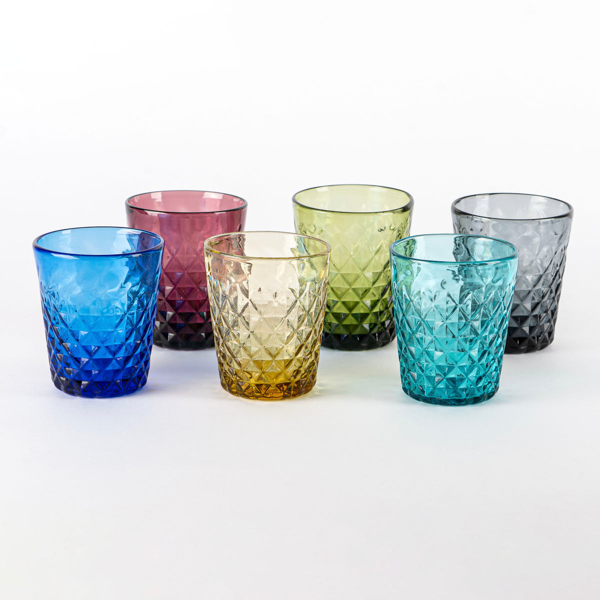 six verres en verre transparent facettés de couleurs différentes sur fond blanc, bleu, violet, jaune, vert, turquoise et gris