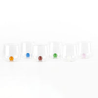Set di sei bicchieri trasparenti con base doppia, ciascuno contiene una sfera colorata diversa: arancione, blu, rossa, verde, bianca e rosa, su