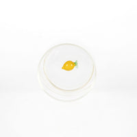 bicchiere trasparente con interno decorato da piccolo limone giallo e due foglie verdi visto dall'alto su sfondo bianco