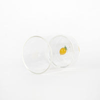 bicchiere trasparente in vetro con piccolo limone decorativo giallo e verde sul fondo, su sfondo bianco neutro
