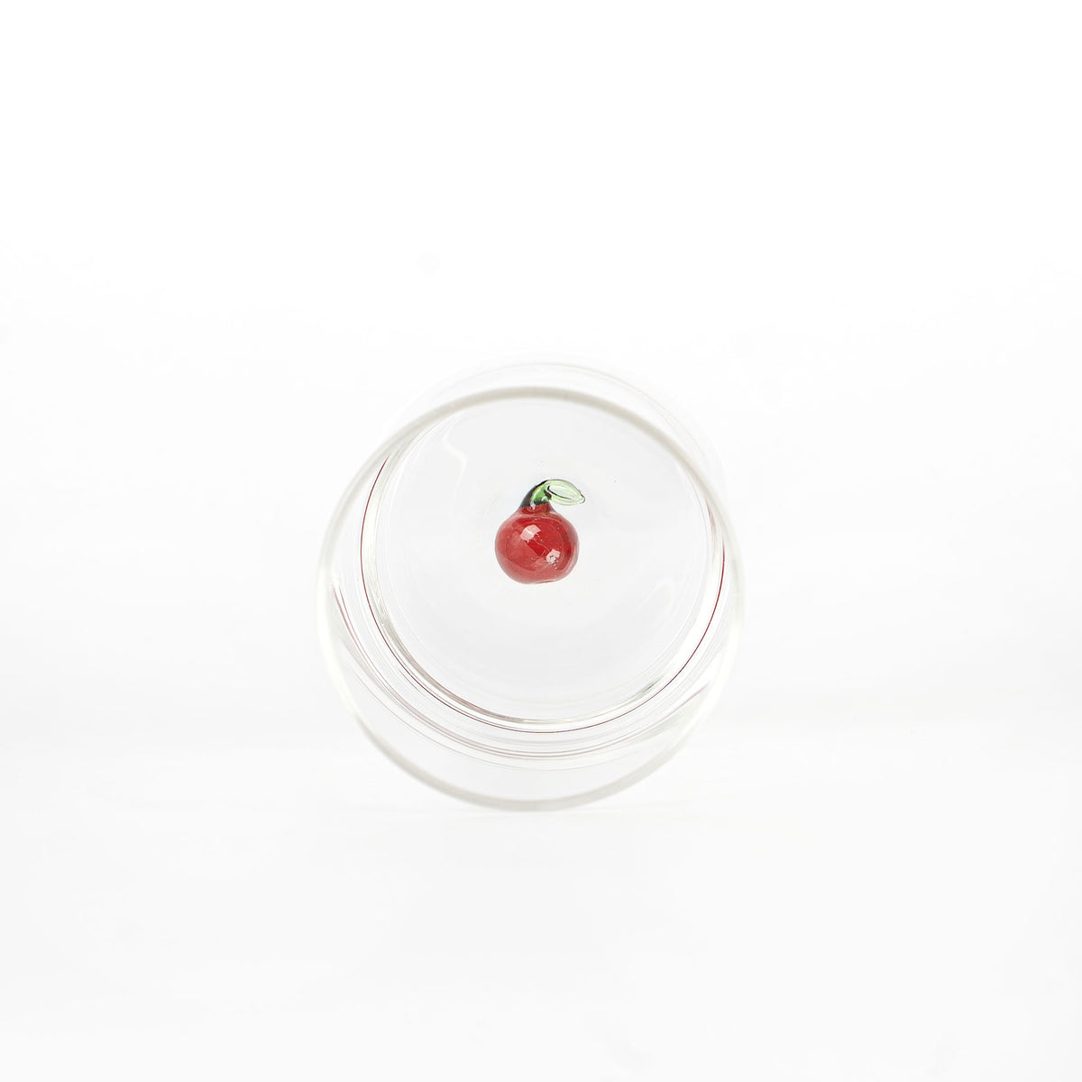 bicchiere trasparente in vetro con ciliegia rossa decorativa e foglia verde sul fondo, sfondo bianco uniforme