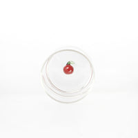 bicchiere trasparente in vetro con ciliegia rossa decorativa e foglia verde sul fondo, sfondo bianco uniforme