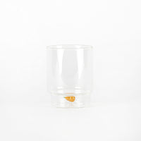 bicchiere trasparente di vetro con carota arancione decorativa sul fondo, sfondo bianco uniforme