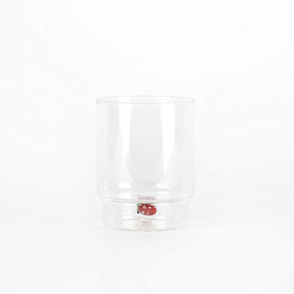Bicchiere trasparente in vetro con base rialzata e decorazione a forma di fragola rossa con punti bianchi interna su sfondo bianco.