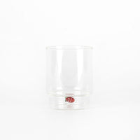 Bicchiere trasparente in vetro con base rialzata e decorazione a forma di fragola rossa con punti bianchi interna su sfondo bianco.
