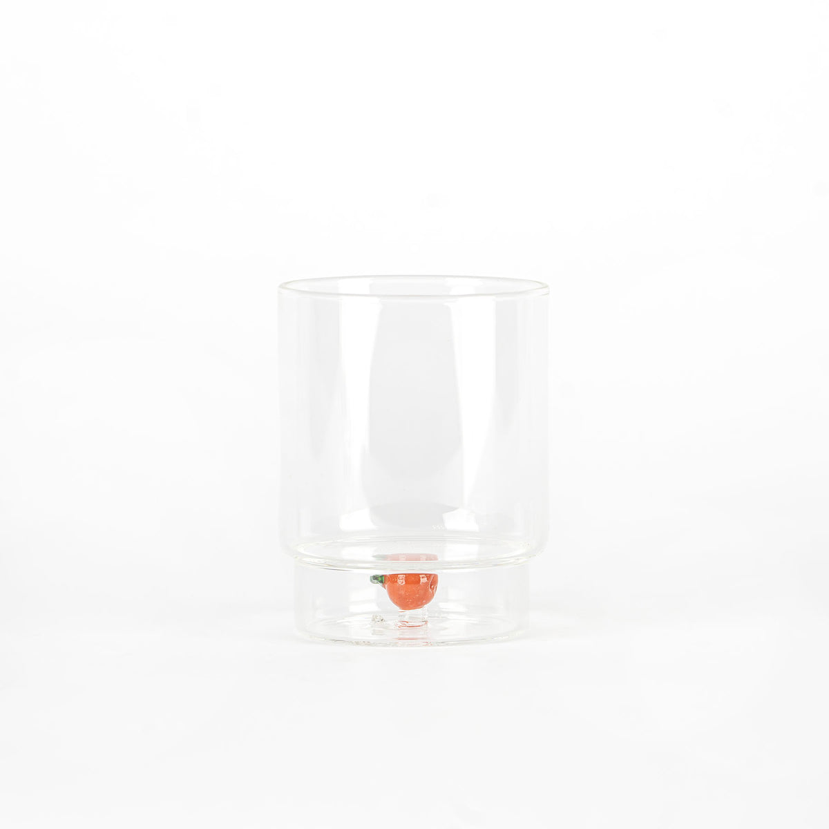 bicchiere trasparente in vetro con forma cilindrica e piccolo pomodoro decorativo sul fondo, sfondo bianco neutro