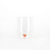 bicchiere trasparente in vetro con forma cilindrica e piccolo pomodoro decorativo sul fondo, sfondo bianco neutro