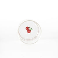 bicchiere di vetro trasparente con decorazione interna di ciliegie rosse con foglie verdi su sfondo bianco
