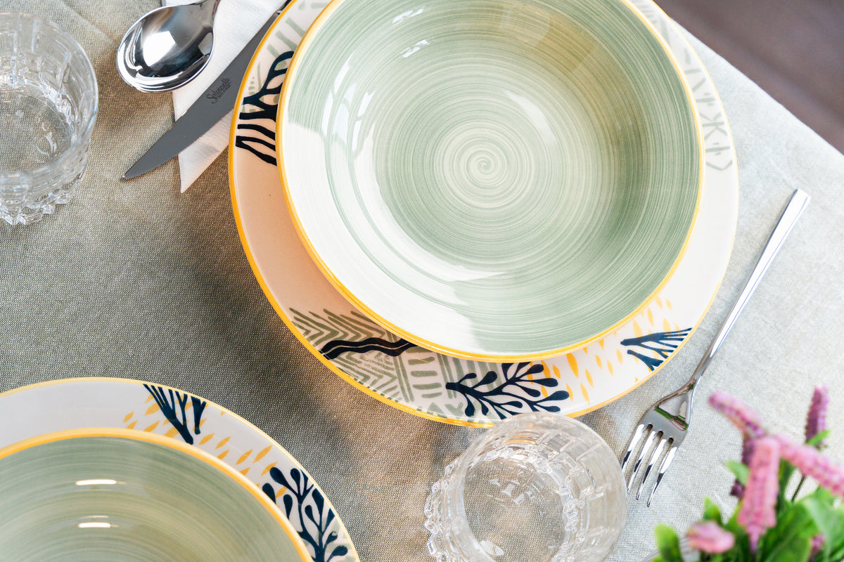 Ceramic bowls with decorative patterns on light tablecloth, stainless steel cutlery, clear glass and flowers in background.
