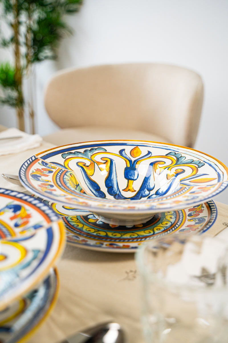 Decorated plate with blue, yellow and orange patterns, on a table with a light tablecloth and metal cutlery.