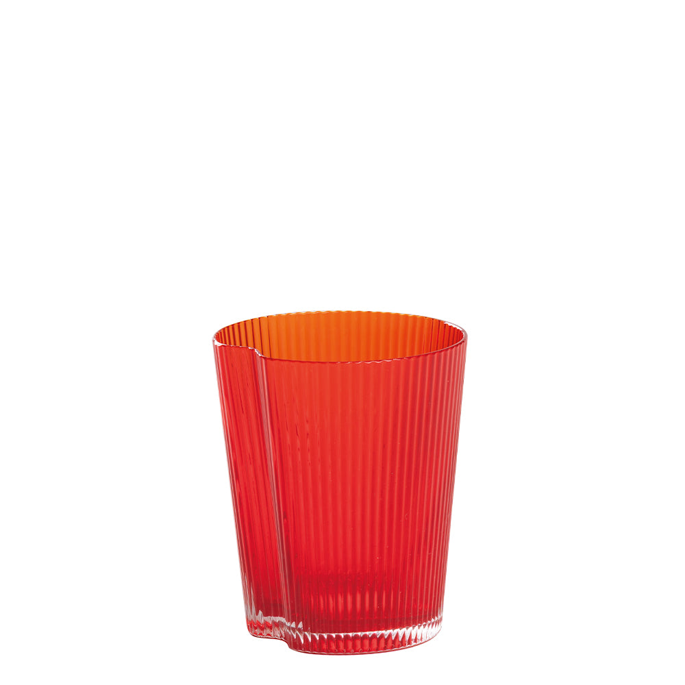 Vaso transparente rojo de cristal con superficie estriada y borde superior irregular sobre fondo blanco