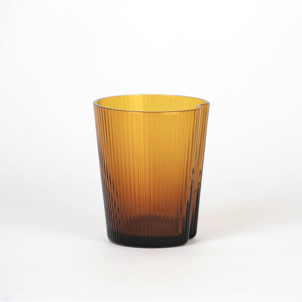 Vaso de vidrio transparentee ámbar color csobre vertical ribbed surface y smooth top rim, sobre fsobredo blanco.