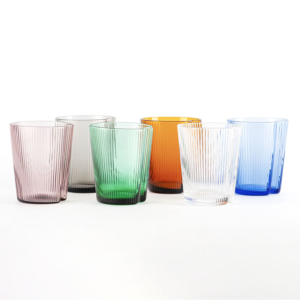 Seis vasos de vidrio transparente coloreados con superficies estriadas, en rosa, gris, verde, naranja, transparente y azul sobre fondo blanco.