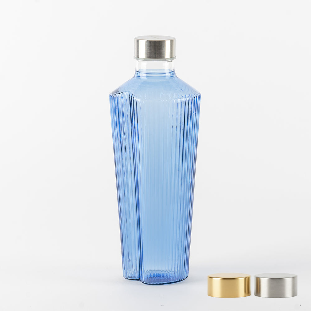 Hellblaue transparente Glasflasche mit gerillter Oberfläche, silbernem Metallverschluss und zwei Ersatzverschlüssen in Gold und Silber auf weißem Hintergrund.