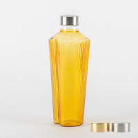 Gelbe Glasflasche mit geriffelten Oberflächen und silbernem Metallverschluss, mit zwei zusätzlichen gold- und silberfarbenen Verschlüssen auf weißem Hintergrund.