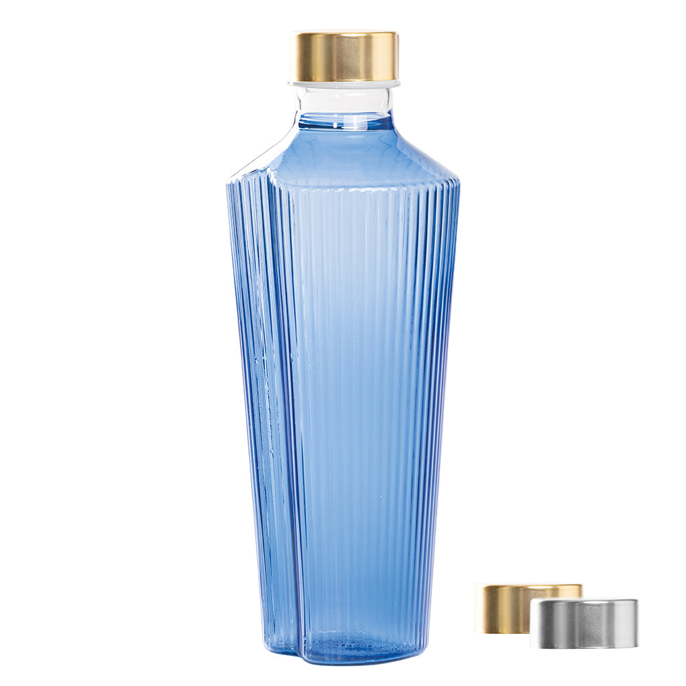 Blaue Glasflasche mit gerillter Oberfläche, goldenem Verschluss und Silber daneben. Weißer Hintergrund.