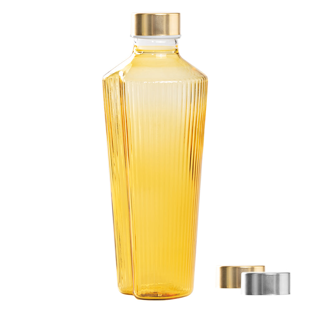 Winklige transparente Plastikflasche mit gelber Flüssigkeit, goldenem Verschluss und goldenen und silbernen Metallverschlüssen daneben.
