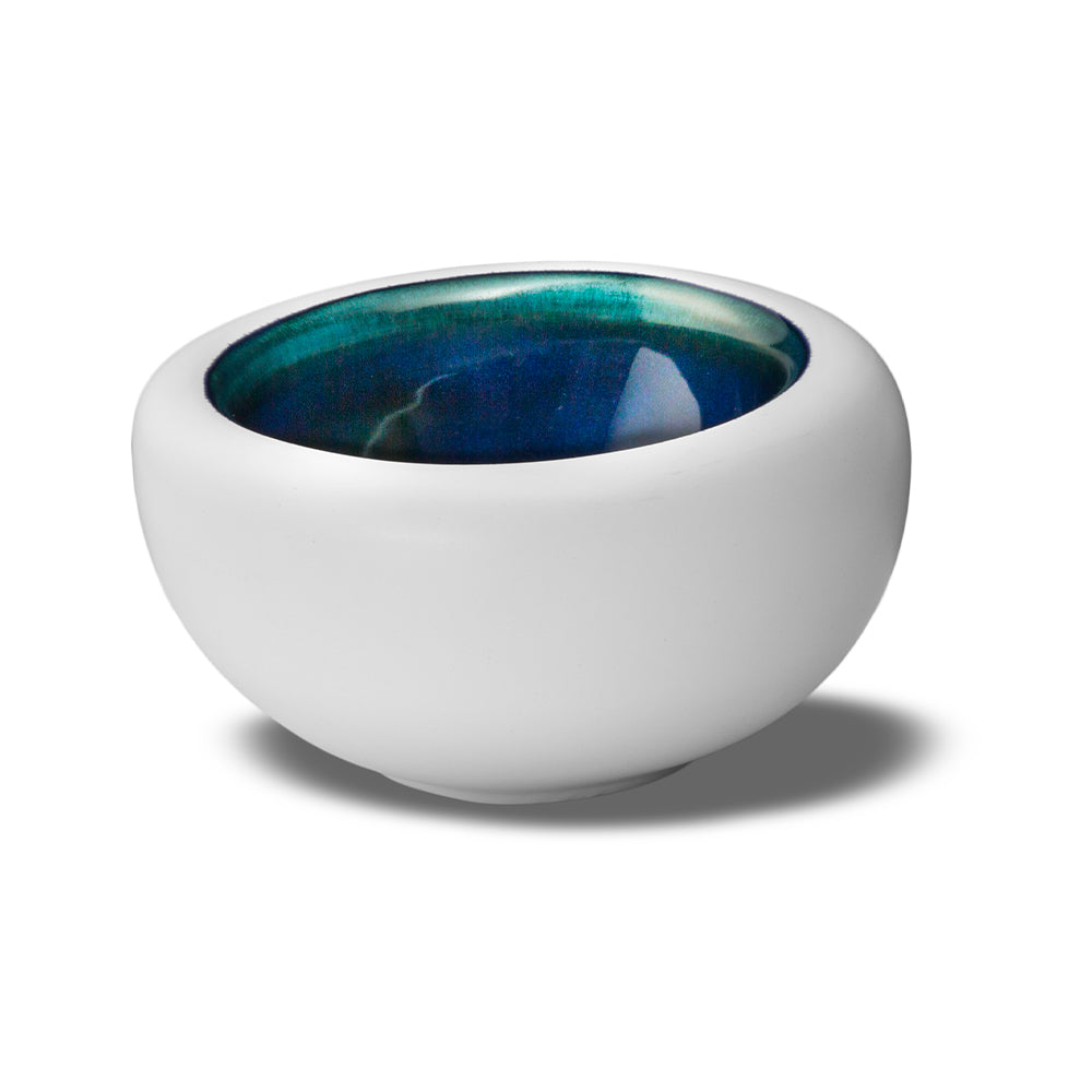 Ronde witte kom met glanzend geglazuurd interieur in blauw en groene tinten, op neutrale witte achtergrond.