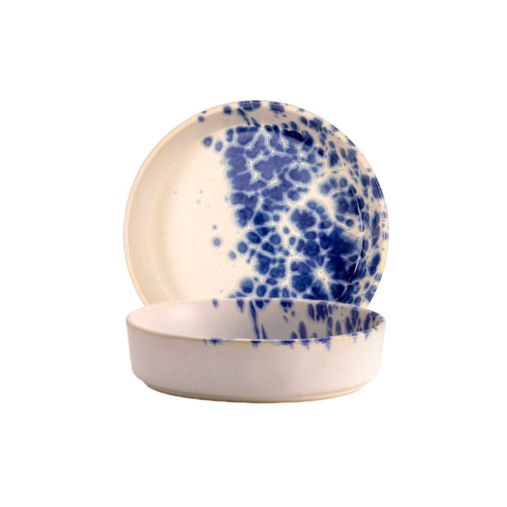 Due piatti rotondi in ceramica color crema con decorazioni blu a macchie, uno fondo e uno piano appoggiato dietro.