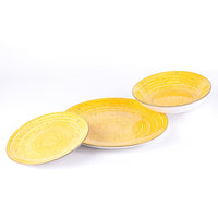 Tre piatti di ceramica gialla, con motivi a spirale e puntini neri, su sfondo bianco. Due piatti sono circolari e uno è profondo.
