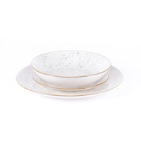 Set de platos de cerámica blanca con superficie manchada negra y bordes dorados, compuesto por un plato y un cuenco.