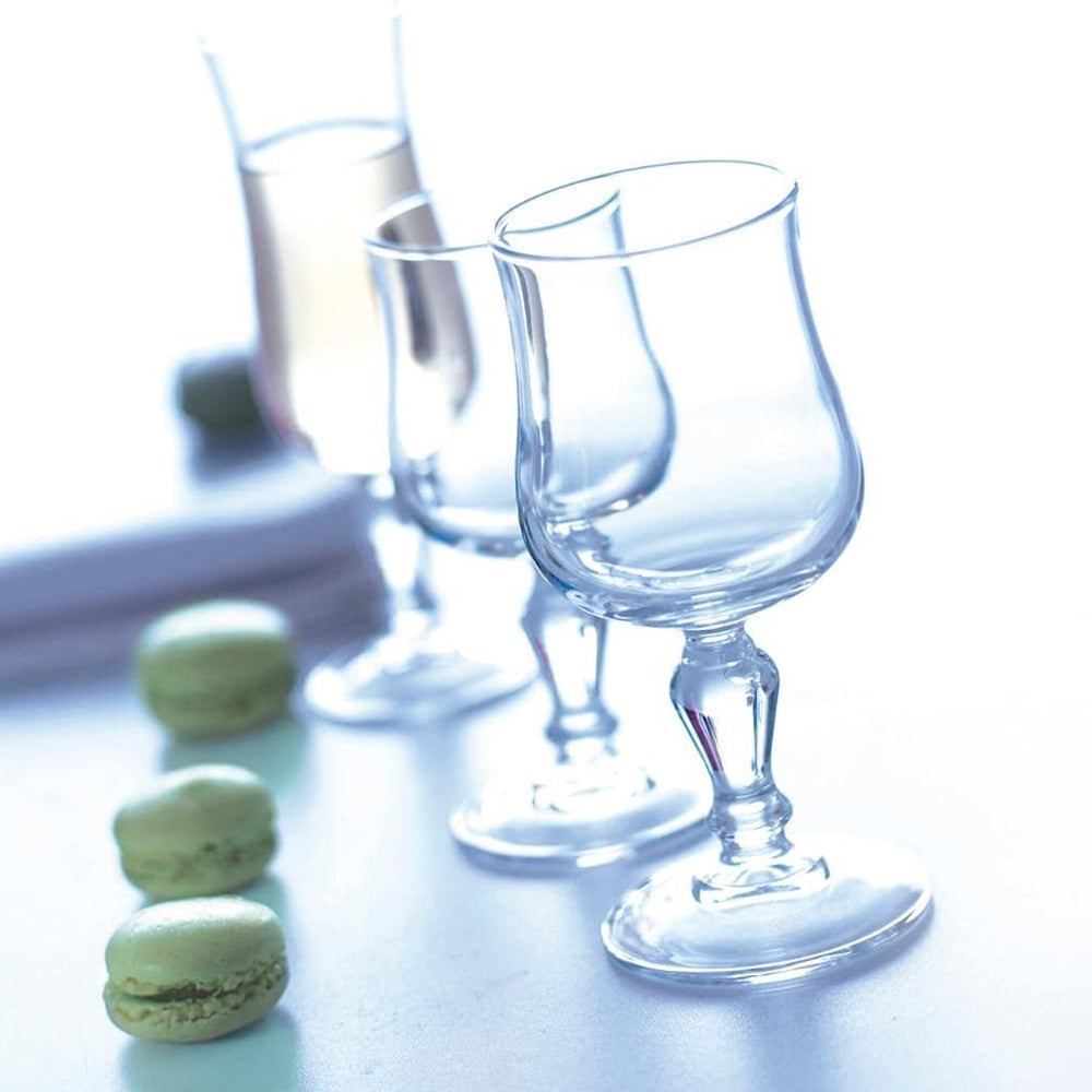 Tres vasos de vidrio transparente sobre superficie clara, acompañados de tres macarons verdes. Ligero desenfoque al fondo.