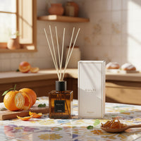 Diffuseur d'ambiance en verre ambré avec bâtonnets en bois, à côté d'une boîte blanche avec inscription CULTI MILANO, sur table avec carreaux colorés et