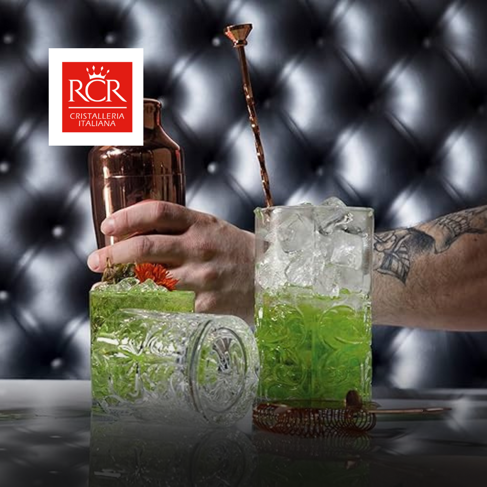 due bicchieri decorati in vetro trasparente con cocktail verde e ghiaccio e mano con shaker rame su sfondo