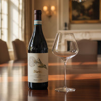 Vietti Langhe Nebbiolo Perbacco red wine bottle with white label and clear glass wine glass on wooden table in elegant interior.