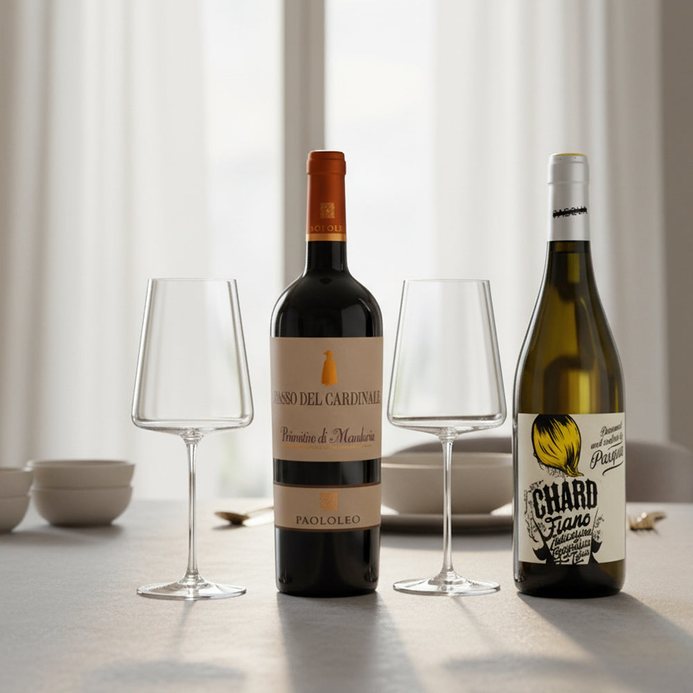 Due bottiglie di vino, una rossa Passo del Cardinale Primitivo di Manduria con etichetta beige e una bianca Chard Fiano con etichetta illustrata, e