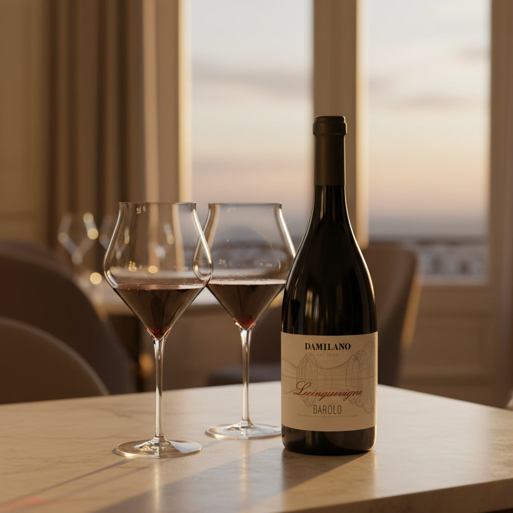 Bouteille de vin rouge Damilano Leinquecingno Barolo à côté de deux calices à moitié pleins sur table claire avec fond intérieur et fenêtre.