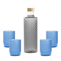 Bottiglia trasparente con tappo dorato e quattro bicchieri blu, con motivo a piramide, su sfondo bianco.