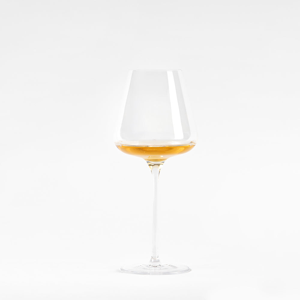Calice di vino trasparente con gambo lungo, contenente liquido dorato, su sfondo bianco.